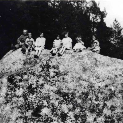 Augusti 2023. Syskonen Felix, Bruno, Irma, Hanna, Helena, Greta och Julia Dahlgren på "Storsten" sommaren 1929. Stenen fanns ovanför vägen och hälften sprängdes bort vid vägomläggningen på 1930-talet och resten när vägen breddades 1959.